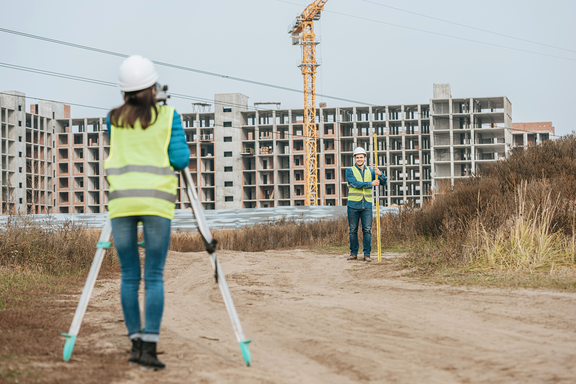 Surveyors measuring land on dirt road with construction site at background