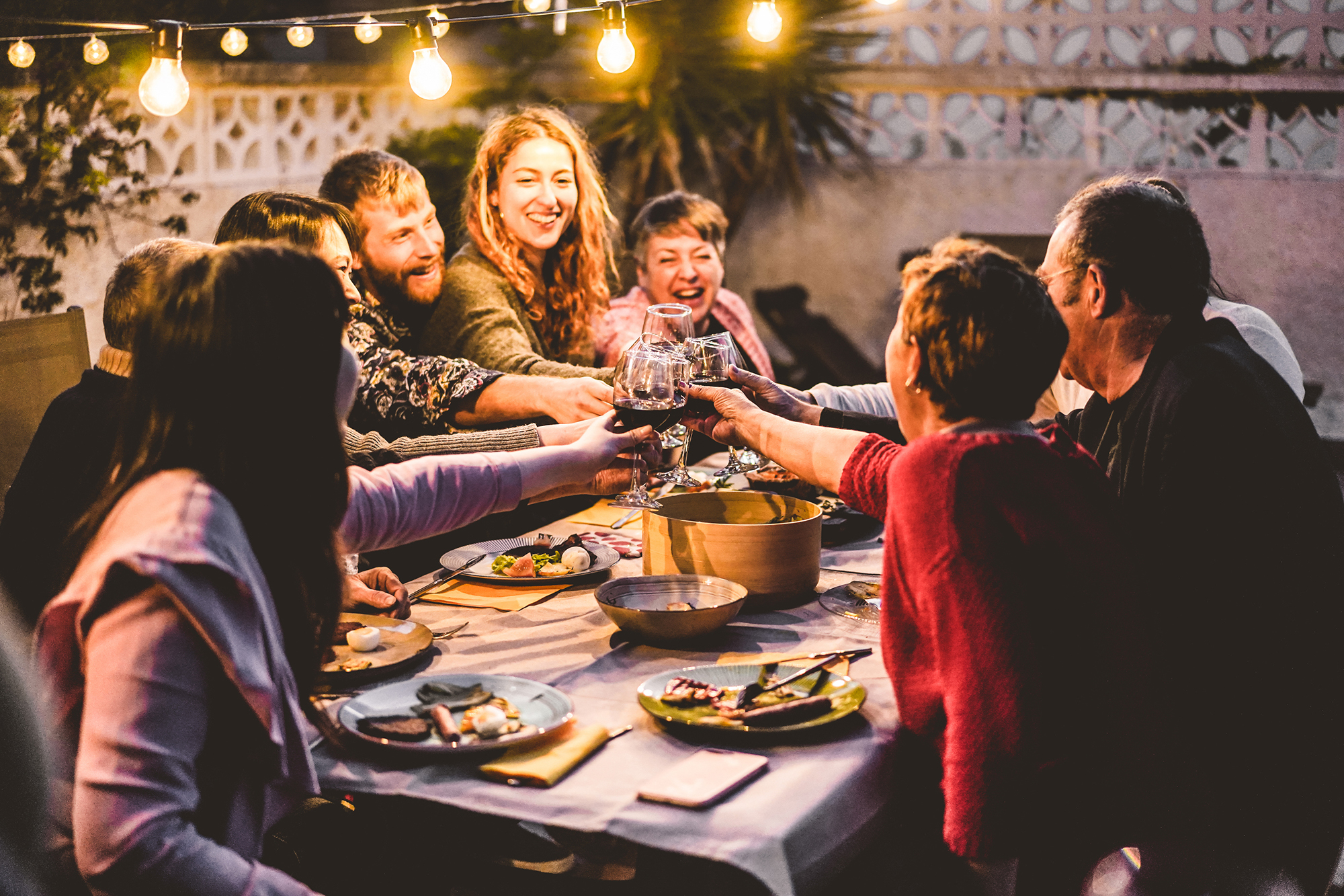 Happy family cheering with red wine at barbecue dinner outdoor - Different age of people having fun at weekend meal - Food, taste and summer concept - Focus on hands toasting